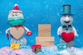 Two cheerful snowmen are standing in the snow, next to boxes with gifts and a wooden pedestal