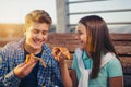 Two cheerful teenagers, girl and boy, eating pizza