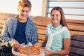 Two cheerful teenagers, girl and boy, eating pizza outdoor