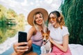 Two cheerful woman friends resting outdoor on lake pier with dog, making photo, selfie Royalty Free Stock Photo