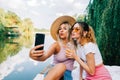 Two cheerful woman friends resting outdoor on lake pier, making photo, selfie Royalty Free Stock Photo