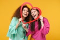 Two cheerful women friends european and african american girls in pink green clothes posing isolated on yellow wall Royalty Free Stock Photo