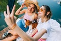 Two cheerful women friends resting outdoor on lake pier with dog, making photo, selfie Royalty Free Stock Photo