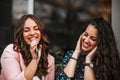 Two cheerful women listening music with cellphone and earphones and singing while sitting in the sitting on the city street Royalty Free Stock Photo