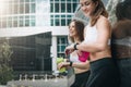 Two cheerful women runners stand leaning against trailer, rest after training, drink water, looking on pulsometer.