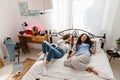 Two cheerful young girls holding brushes as microphones and singing songs while lying in bed together Royalty Free Stock Photo