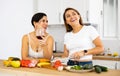 Two cheerful female roommates drinking wine and preparing dinner at home