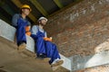 Two cheerful young male builders in blue overalls and hard hats sitting on the concrete floor, taking a break, drinking Royalty Free Stock Photo