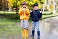 Two cheerfull boys in rubber boots standing in puddle in park. Concept of social adaptation of autistic children