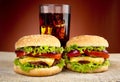 Two cheeseburgers,glass of cola on wooden table on red spotlight