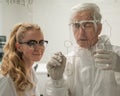 Two chemist colleagues write formulas on glass. Caucasian elderly man and young woman brainstorming. Royalty Free Stock Photo