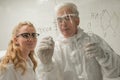 Two chemist colleagues write formulas on glass. Caucasian elderly man and young woman brainstorming. Royalty Free Stock Photo