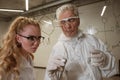 Two chemist colleagues write formulas on glass. Caucasian elderly man and young woman brainstorming. Royalty Free Stock Photo