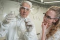 Two chemist colleagues write formulas on glass. Caucasian elderly man and young woman brainstorming. Royalty Free Stock Photo