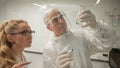 Two chemist colleagues write formulas on glass. Caucasian elderly man and young woman brainstorming. Royalty Free Stock Photo