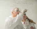 Two chemist colleagues write formulas on glass. Caucasian elderly man and young woman brainstorming. Royalty Free Stock Photo