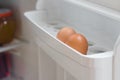 Two chicken eggs on a shelf of the refrigerator door open closeup