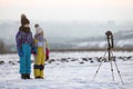 Two children boy and girl having fun outside in winter playing with photo camera on a tripod on snow covered field Royalty Free Stock Photo