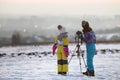 Two children boy and girl having fun outside in winter playing with photo camera on a tripod on snow covered field Royalty Free Stock Photo