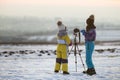 Two children boy and girl having fun outside in winter playing with photo camera on a tripod on snow covered field Royalty Free Stock Photo