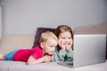 Two children a boy and a girl lie on a sofa in home clothes and watch videos on a laptop Royalty Free Stock Photo