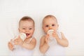 Two children a boy and a girl-twins of 8 months drink milk from a bottle on the bed in the nursery, feeding the baby, baby food Royalty Free Stock Photo