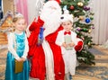 Two children dressed in carnival suits with Santa Claus near christmas fir tree