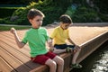 Two children feed the wild ducks and shoal of small fish in azure clean transparent lake. Brother boys are best friends. Summer Royalty Free Stock Photo