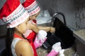 Two children girls wash dishes and laptop in sink on kitchen. Wearing red uniform of cook with hat and apron.