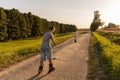 Two children are having fun inline skating on a wide, unpaved path through a scenic area filled with trees. The sun sets, creating Royalty Free Stock Photo