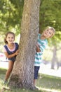 Two Children Hiding Behind Tree In Park