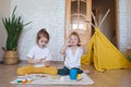 Two children in light clothes sit on the floor on their knees and enthusiastically draw with bright watercolors.