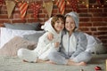 Two children in pajamas sitting on the bed waiting for Christmas gifts.