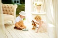 Two children play on floor in summer pavilion in garden. Brother and sister spend time together. Boy in white summer hat with toy Royalty Free Stock Photo