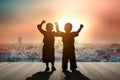 Two children raise their hands on a wooden balcony in the city.