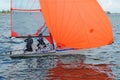 Two children sailing a racing dinghy with a large fully deployed orange coloured spinnaker