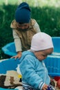 Two children sit in the sandbox and play with shovels, rakes, toys Royalty Free Stock Photo