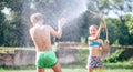 Two childs, brother and sister, have fun, when play with watering hose in summer garden Royalty Free Stock Photo