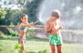 Two childs playing in garden, pours each other from the hose, makes a rain. Happy childhood concept image Royalty Free Stock Photo