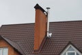 Two chimneys made of brown bricks and gray metal on the tiled roof of a private house Royalty Free Stock Photo