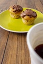 Two chocolate chip muffins on a yellow plate and white cup of tea and wooden table . Copy space. Premium quality bakery product Royalty Free Stock Photo