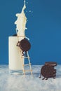 Two chocolate cookies climb stairs into glass of milk on blue paper background. Creative concept. Still life Royalty Free Stock Photo