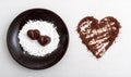 Two chocolate heart-shaped candies on a brown plate with sugar powder next to chocolate chips arranged into a heart shape Royalty Free Stock Photo