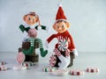 Two Christmas Elves with Red and Green Outfits Sitting on Wood, holding large pieces of candy with more candy scattered around.