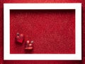 Two Christmas toys in the shape of a heart lie in a white frame on a red shiny background.