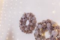 Two Christmas wreath made from pine cones with shiny garland lights hanging on white wall, copy space. Winter holidays, New Year Royalty Free Stock Photo