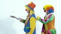 Two circus clowns throwing up a toy- pancake and catching it usin frying pans
