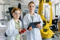Two classmates standing in robotic laboratory, wearing lab coats and safety eyeglasses. After-school robotics club