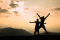 Two climbers in silhouette stand on a beautiful mountain with their hands raised against an orange sky background Royalty Free Stock Photo