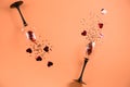 Two clinking wine glasses poured out red heart confetti on orange color paper background. Minimal style. Royalty Free Stock Photo